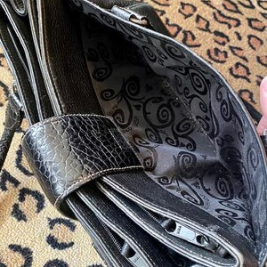 K&ouml;nnte beinhalten: Schwarze Ledertasche mit Rei&szlig;verschluss und gemustertem Futter. Die Tasche hat einen oberen Griff und einen abnehmbaren Schultergurt.