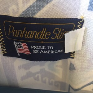 May include: A blue label with gold lettering that reads "Panhandle Slim" and "Proud to be American". The label also features a small American flag.