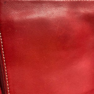 May include: Close-up of a red leather surface with a subtle texture. The leather has a smooth, even finish and appears to be high quality.