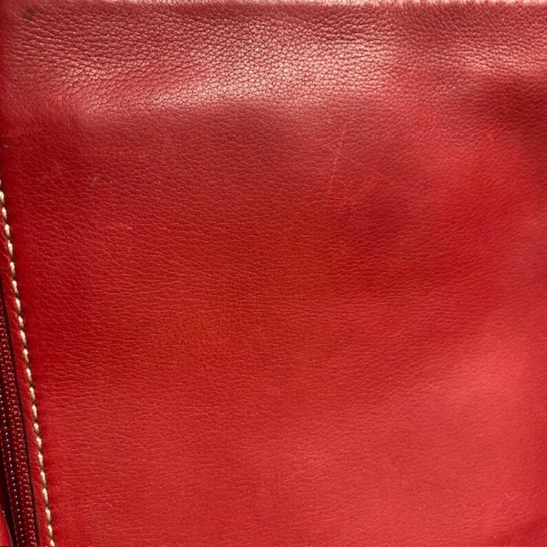 May include: Close-up of a red leather surface with a subtle texture. The leather has a smooth, even finish and appears to be high quality.