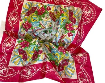 May include: A pink cotton bandana with a white center featuring a floral pattern with blue, yellow, and green accents. The bandana has a scalloped edge with a white floral design.