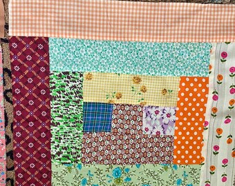 Può includere: Una trapunta patchwork con una varietà di tessuti colorati, tra cui arancione, verde, blu e rosso. La trapunta è composta da quadrati e rettangoli di diverse dimensioni e motivi.