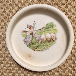 Könnte beinhalten: Ein weißer Keramikteller mit einer bunten Illustration eines Mädchens in einem grün-blauen Kleid, das Schafe hütet. Der Text "Little Bo-Peep" ist auf dem Teller gedruckt.