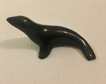 May include: A black ceramic seal figurine. The seal is in a swimming pose with its head turned to the left.
