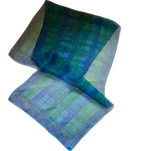 May include: A sheer, square scarf with a plaid pattern in shades of blue and green. The scarf has a light blue border and a soft, flowing appearance. The fabric appears to be silk or a similar lightweight material.