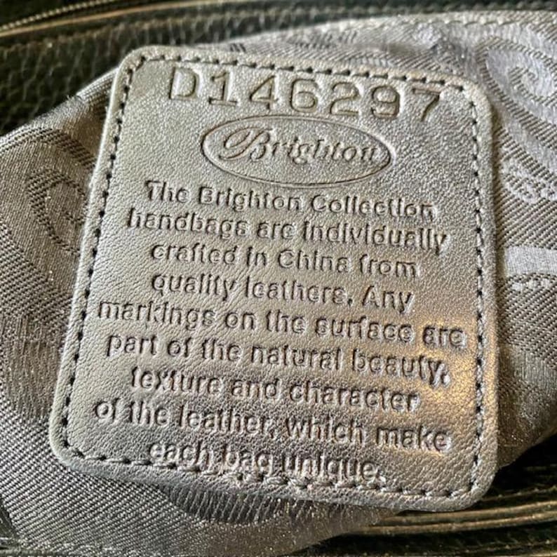K&ouml;nnte beinhalten: Nahaufnahme eines schwarzen Leder-Handtaschenetiketts mit dem Text "D146297 Brighton The Brighton Collection handbags are individually crafted in China from quality leather. Any markings on the surface are part of the natural beauty. Texture and character of the leather, which make each bag unique."