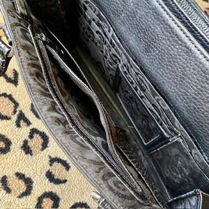 K&ouml;nnte beinhalten: Das Innere einer schwarzen Lederhandtasche mit einem Rei&szlig;verschlussfach und einem gemusterten Futter.