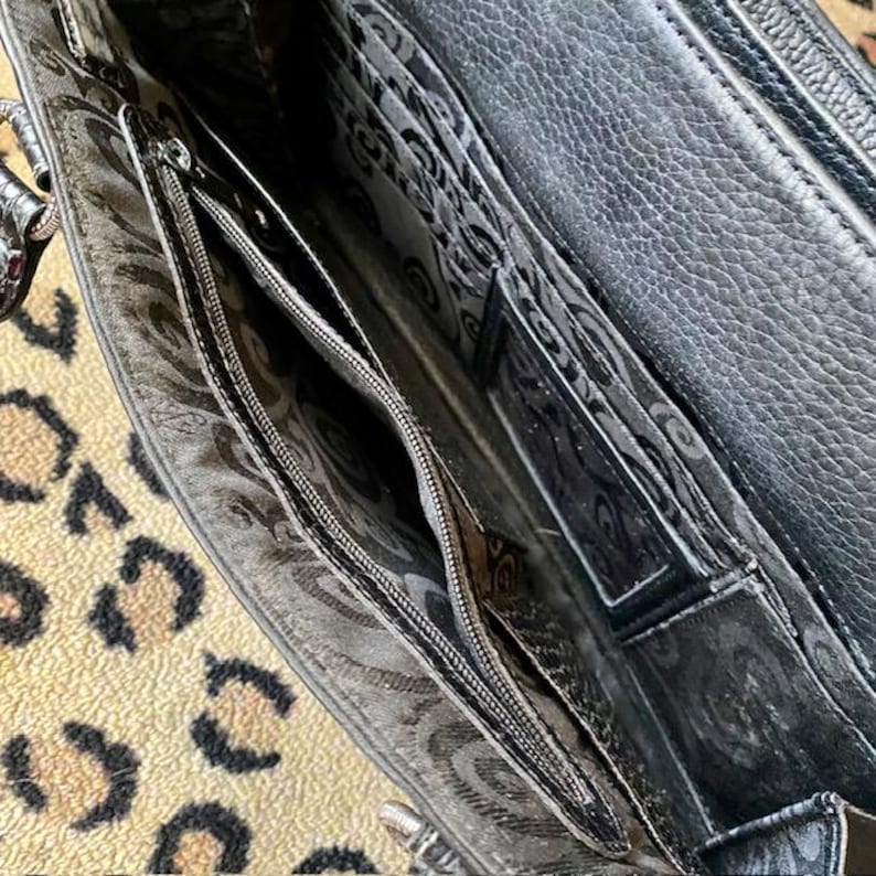 K&ouml;nnte beinhalten: Das Innere einer schwarzen Lederhandtasche mit einem Rei&szlig;verschlussfach und einem gemusterten Futter.