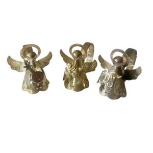 May include: Three metal angel figurines with outstretched wings and halos. One angel holds a small instrument. The angels are in varying shades of gold and silver, with intricate details on their wings and bodies.