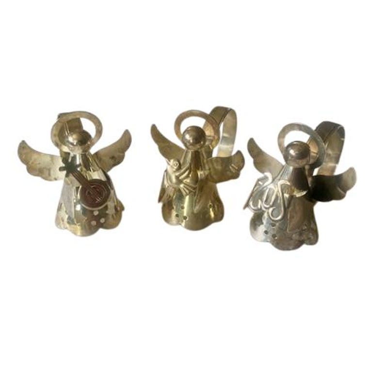 May include: Three metal angel figurines with outstretched wings and halos. One angel holds a small instrument. The angels are in varying shades of gold and silver, with intricate details on their wings and bodies.