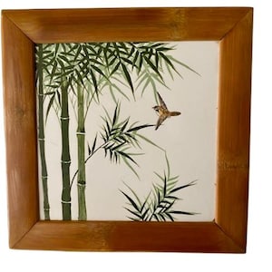 Puede incluir: Obra de arte cuadrada enmarcada en bambú, que representa tallos y hojas de bambú en tonos verdes, con un pequeño pájaro marrón en vuelo. El fondo es blanco.