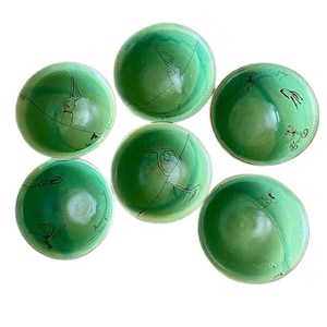 Puede incluir: Seis cuencos de cerámica verde con dibujos de figuras en línea negra sobre fondo blanco. Los cuencos son todos del mismo tamaño y forma.