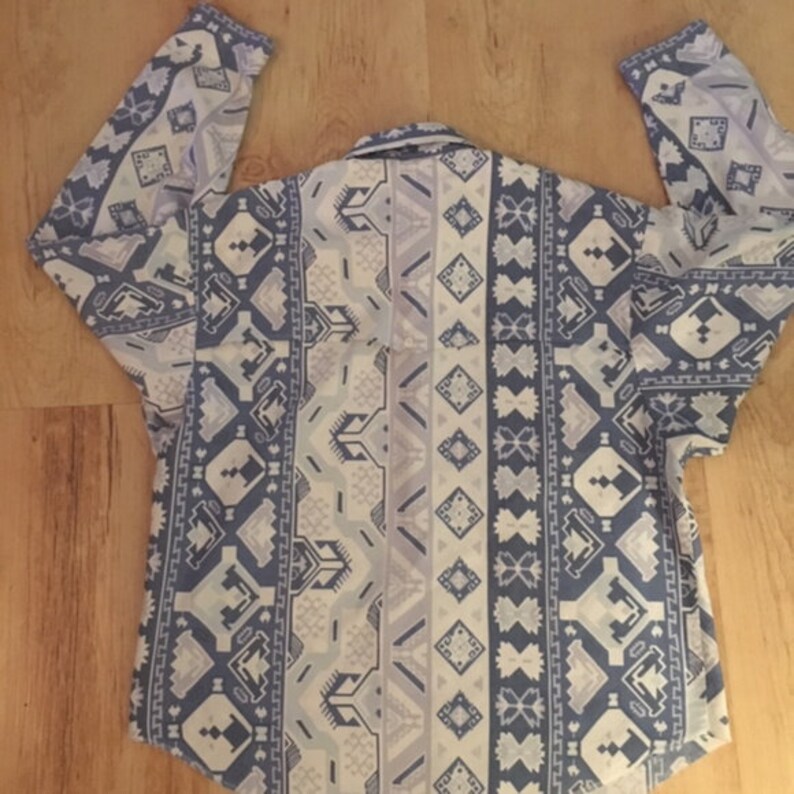 May include: A long-sleeved shirt with a white and blue geometric pattern. The pattern features a variety of shapes, including diamonds, triangles, and squares.