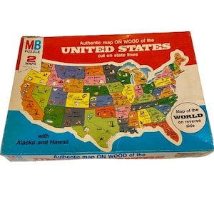 May include: A vintage MB Puzzle featuring a colorful map of the United States, cut along state lines. The box is blue, red, and white, with text indicating it includes two maps and a world map on the reverse side. The puzzle includes Alaska and Hawaii.