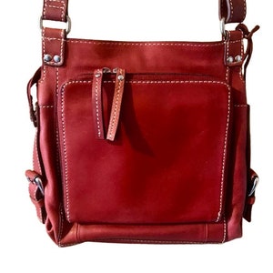 May include: A red leather crossbody bag with a zippered pocket and a flap closure. The bag has a white stitch detail and silver hardware.