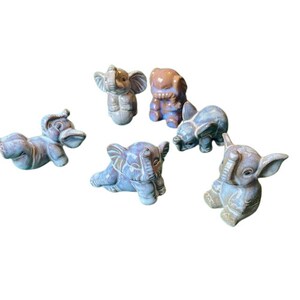 May include: A collection of six ceramic elephant figurines in various shades of blue and purple. The elephants are in different poses, some standing, some lying down, and some sitting.