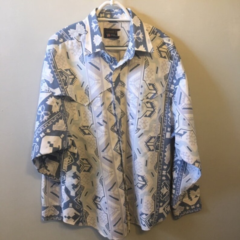 May include: A long-sleeved button-down shirt with a geometric pattern in shades of blue, white, and gray. The shirt has a pointed collar and a single button closure.