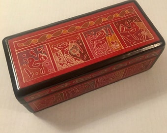 May include: A rectangular wooden box with a red lid decorated with a colorful pattern of stylized animals. The box is closed.