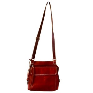 May include: A red leather crossbody bag with a long adjustable strap and multiple pockets.