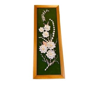 May include: A framed floral artwork featuring white shell flowers and accents on a dark green background. The artwork is encased in a gold-colored wooden frame, creating a decorative piece for wall decor.
