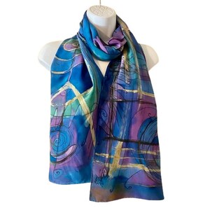 May include: A blue silk scarf with an abstract design in shades of purple, green, and gold. The design features swirls, lines, and geometric shapes.
