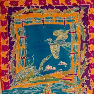 May include: A colorful silk scarf with a blue background featuring two herons, one flying and one standing on a green and yellow landscape. The border is a repeating pattern of orange, yellow, purple, and pink fish and frogs.