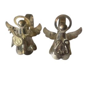 May include: Two silver-coloured angel figurines. One angel holds a small instrument, while the other has a decorative design on its body. Both have halos and wings, and are designed to hang.