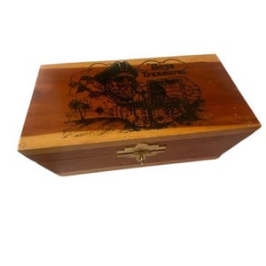 Può includere: Forziere in legno con un'illustrazione di pirata e la scritta "Boys Treasures". Il forziere è rettangolare con un coperchio incernierato e una chiusura in metallo. Il legno ha un tono caldo e naturale.