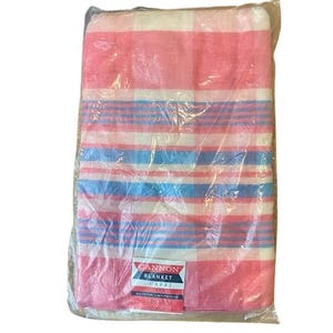 Peut inclure: Une couverture rayée rose et bleue avec les mots "Cannon Blanket Capri" imprimés en bas à droite. La couverture est emballée dans du plastique.