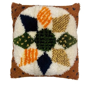 May include: A brown and white throw pillow with a colorful, geometric design. The design features a starburst pattern with shades of green, orange, black, and brown.