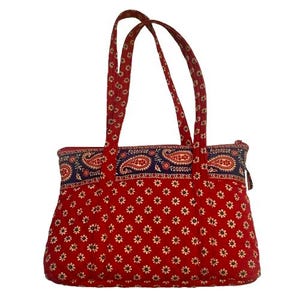 Puede incluir: Un bolso tote acolchado rojo con un estampado floral. El bolso presenta una banda azul marino con un diseño de cachemira en la parte superior y asas rojas a juego. El bolso tiene un cierre de cremallera.