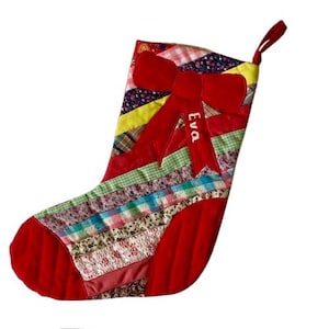 May include: A patchwork Christmas stocking with a red bow and the name "Eva". The stocking is made from various patterned fabrics in shades of red, blue, green, and yellow. A loop is attached for hanging. The overall design is festive.