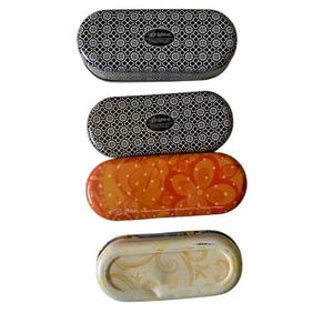 May include: Four oval-shaped eyeglass cases. Two cases have a black and white geometric pattern with the brand name "Brighton". One case is orange with a floral design. The last case is white with a yellow floral design.