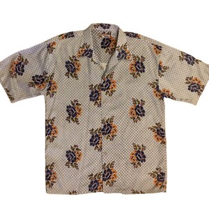 May include: A short-sleeved, light blue button-up shirt with a floral pattern. The flowers are a mix of orange, purple, and green.