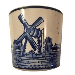 May include: A white ceramic mug with a blue and white windmill scene. The mug features a windmill with a blue and white design, trees, and a house.
