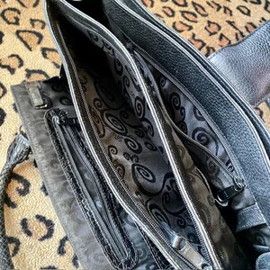 K&ouml;nnte beinhalten: Schwarze Ledertasche mit mehreren F&auml;chern und Rei&szlig;verschluss. Die Tasche hat ein gemustertes Futter.