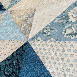 May include: Close-up of a patchwork quilt with various blue and cream floral and patterned fabrics. The quilt is made of triangular pieces, stitched together with decorative quilting.