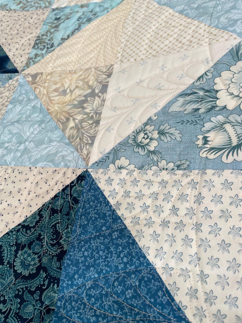 May include: Close-up of a patchwork quilt with various blue and cream floral and patterned fabrics. The quilt is made of triangular pieces, stitched together with decorative quilting.