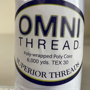 May include: A spool of white OMNI THREAD, a poly-wrapped poly core thread. The label reads "SUPERIOR THREADS" and "6,000 yds. TEX 30". The spool is cylindrical and appears to be new.