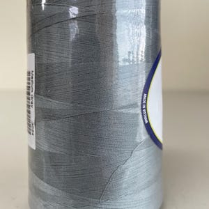 May include: A large cylindrical spool of medium gray sewing thread wrapped in clear plastic film. A white label on the side displays the text Medium Gray and 3024, while another label on the right side includes the text Made in Vietnam.