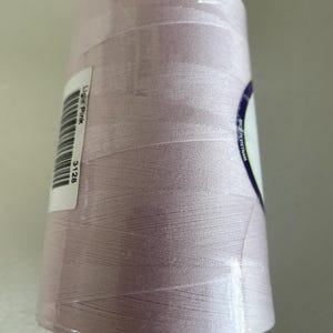 May include: A large spool of light pink sewing thread wrapped in clear plastic film. A white rectangular label is attached to the side, featuring a barcode, the text Light Pink, and the number 3128. A partial label reads Made in Vietnam.