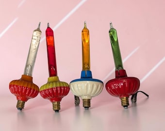 May include: Four vintage bubble light bulbs with metallic screw bases and clips. The bulbs feature clear, red, orange, and green glass tubes atop ribbed, colorful bases in red, yellow, blue, and red, designed for decorative holiday lighting.