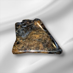 May include: A polished, irregularly shaped gemstone with a swirling pattern of brown, gold, and black hues. The stone has a glossy finish and a unique, organic form, likely for jewelry or display.