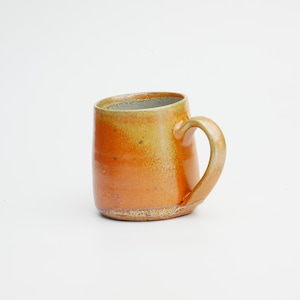 Puede incluir: Una taza de cerámica hecha a mano con un cuerpo redondeado y un asa curva. La taza presenta un degradado de tonos naranja y amarillo, con un interior de color claro. La taza mide aproximadamente 10 cm de alto.