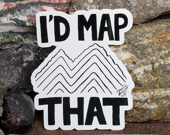 Puede incluir: Una pegatina blanca con texto negro que dice "I'd map that" y una ilustración en blanco y negro de montañas. La pegatina está sobre un fondo de rocas.