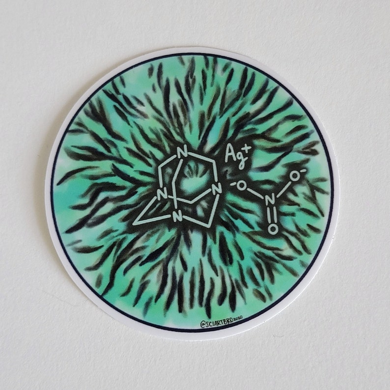 Op de afbeelding: Een ronde sticker met een witte chemische structuur op een turquoise en zwarte achtergrond. De sticker bevat de chemische formule voor zilvernitraat. De handtekening van de kunstenaar, "@SCIARTERO 2020", staat onderaan.