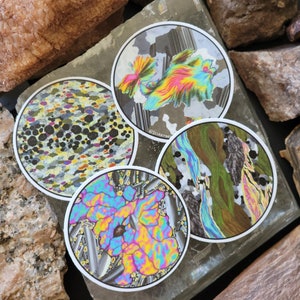 Op de afbeelding: Vier ronde stickers met kleurrijke abstracte patronen. De patronen doen denken aan microscopische afbeeldingen van kristallen of mineralen. De stickers zijn wit met een zwarte rand.