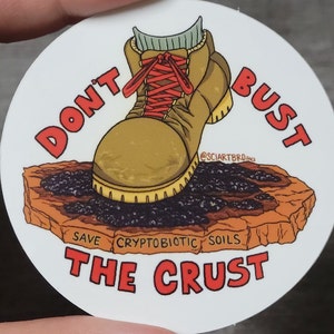May include: A white round sticker with a cartoon illustration of a brown boot stepping on a brown rock with black specks. The boot has red laces and a grey sock. The text on the sticker reads "Don't Bust Save Cryptobiotic Soils The Crust" and "@sciartbro 2023".