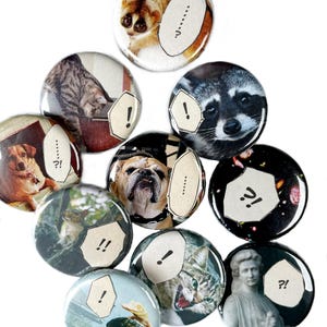 May include: A collection of ten circular pin-back buttons featuring various photographic images including a slow loris, a tabby cat, a raccoon, a dog, a bulldog, a squirrel, a statue, and speech bubbles with punctuation marks like !, ?, and ...