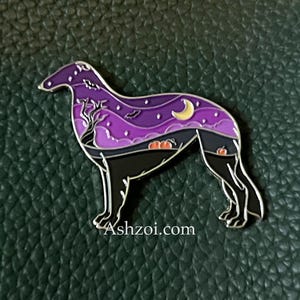 May include: A Halloween-themed enamel pin in the shape of a dog. The pin features a black dog silhouette with a purple and black night sky design inside. The design includes a tree, moon, bats, and pumpkins. The website Ashzoi.com is printed on the pin.